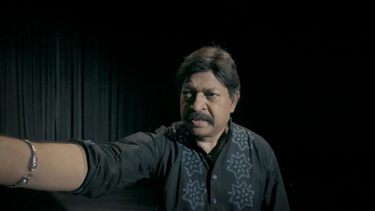 Yash Kirti performs on a dark stage, one arm outstretched