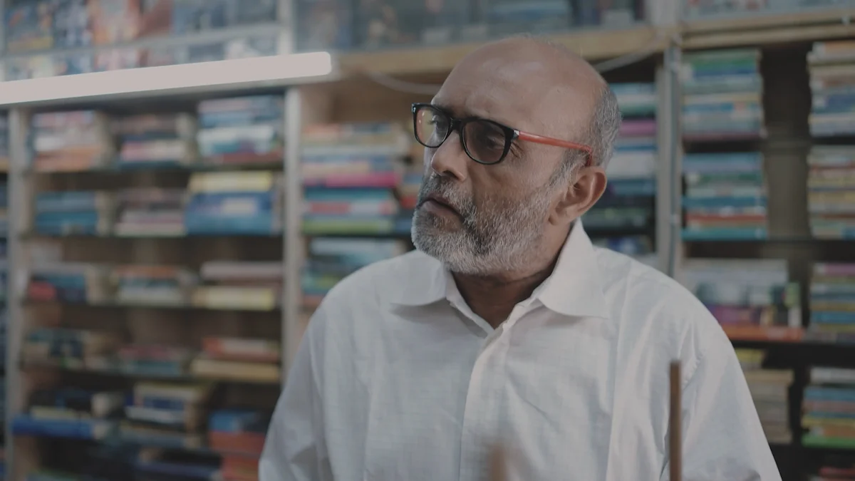 Akbar Hussain as Shamji Bhai, in the bookshop.
