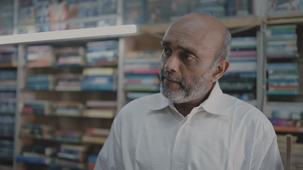 Akbar Hussain as Shamji Bhai, in the bookshop.